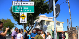 Comitiva em visita ao Bairro Santa Mônica. Placa indica o nome do bairro e da regional Venda Nova. Vereadora Nely Aquino