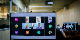 Na tela de um computador, quatro homens e uma mulher fazem reunião remota. 