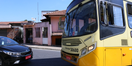 Em uma via asfaltada, ônibus coletivo amarelo parado de frente para carro de passeio, na cor preta