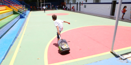 Criança com mochila atravessa pátio de escola, durante o dia. Ao fundo, outros estudantes. 