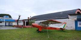 Avião de pequeno porte pousado em gramado de Aeroporto Carlos Prates, durante o dia.