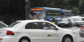 Imagem de um táxi branco em meio ao trânsito da cidade