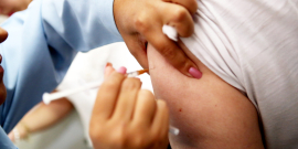 Pessoa caucasiana recebe uma vacina no braço esquerdo