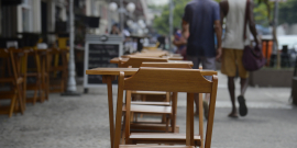 Mesas e cadeiras de bar dispostas em calçada, durante o dia.