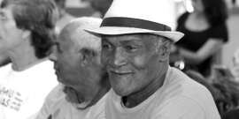 Dois idosos sentados, um deles está com chapéu de palha.