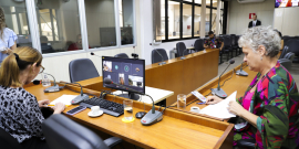 As vereadoras Professora Marli e Cida Falabella estão sentadas no plenário. No computador à frente da Professora Marli, a tela mostra a videochamada em que a vereadora Flávia Borja está presente virtualmente.