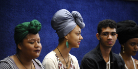 Quatro jovens negros de perfil. As duas mulheres usam turbantes.
