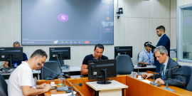 Vereadores discutem projetos no Plenário Camil Caram. O telão atrás deles mostra videochamada com vereadores presentes virtualmente.