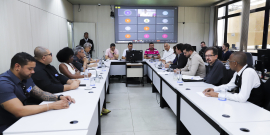 Imagem da reunião com participantes ocupando as cadeiras em torno da mesa em formato de U. O vereador Irlan Melo (Republicanos) está na cabeceira. 