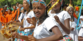 Três mulheres negras dançam vestidas de roupas tradicionais