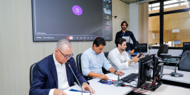 Vereadores estão sentados no plenário. O telão atrás deles mostra a videochamada com parlamentares presentes virtualmente.
