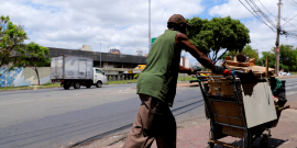 Morador de rua de costas, empurrando carrinho com seus pertences na Praça do Peixe