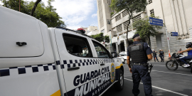 agente da guarda municipal de Belo Horizonte visto de costas ao lado de veículo da corporação