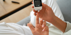 Vista superior de mulher com diabetes verificando seu nível de glicose em um aparelho medidor; ela tem o dedo furado com uma gota de sangue