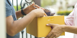 Mãos entregam caixa para pessoa em portão de residência