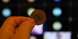 foto de uma mão segurando uma moeda de um real