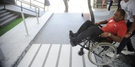 homem cadeirante recebe ajuda de outro homem para subir rampa