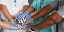 Pessoas vestidas com roupas de médicos e enfermeiros dão as mãos