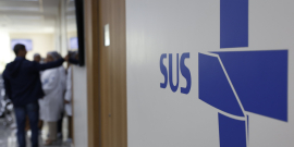 Imagem de corredor de unidade de saúde, com a inscrição SUS na parede