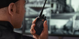 Vigilante aparece de lado, falando em walkie talkie