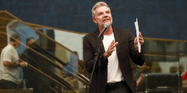 vereador professor juliano lopes discursa tendo microfone à frente e documento nas mãos