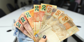 Mão de mulher segura diversas notas em reais