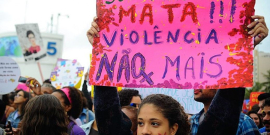 Mulher segura cartaz com os dizeres: "Seu machismo mata!!! Violência não mais"