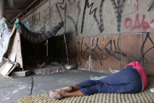 Pessoa em situação de rua deitada na calçada, com barraca de lona ao lado