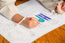 Mãos de criança sobre cartaz ilustrado, colorindo desenhos. Cartaz sobre piso de madeira