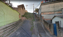 Rua inclinada, com escadaria à direita e uma encosta ao fundo, coberta por vegetação baixa.