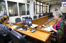 As vereadoras Professora Marli e Cida Falabella estão sentadas no plenário. No computador à frente da Professora Marli, a tela mostra a videochamada em que a vereadora Flávia Borja está presente virtualmente.