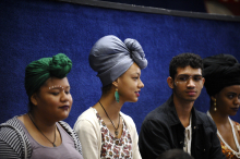 Quatro jovens negros de perfil. As duas mulheres usam turbantes.