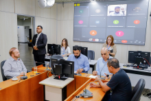 Vereadores estão sentados no plenário Camil Caram. O telão atrás deles mostra a videochamada com um parlamentar presente virtualmente.